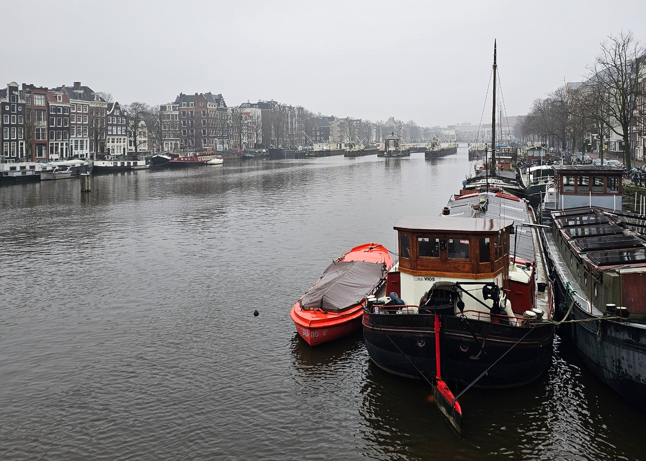 Canal boats on the Amstel, with Amsterdam’s historic buildings lining both banks on a gray winter day.