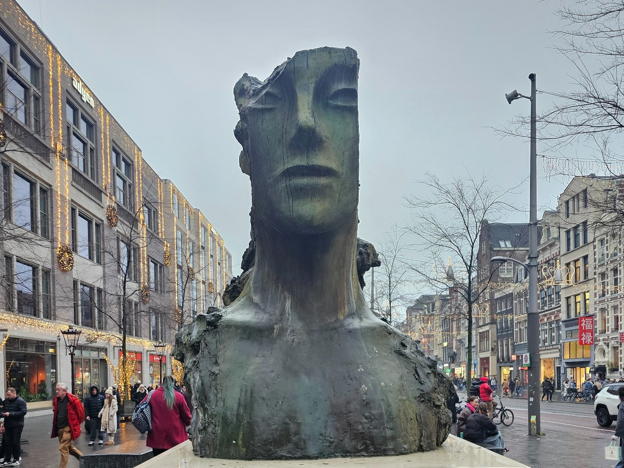 A damaged giant head-and-shoulders sculpture stands on a busy Amsterdam street.