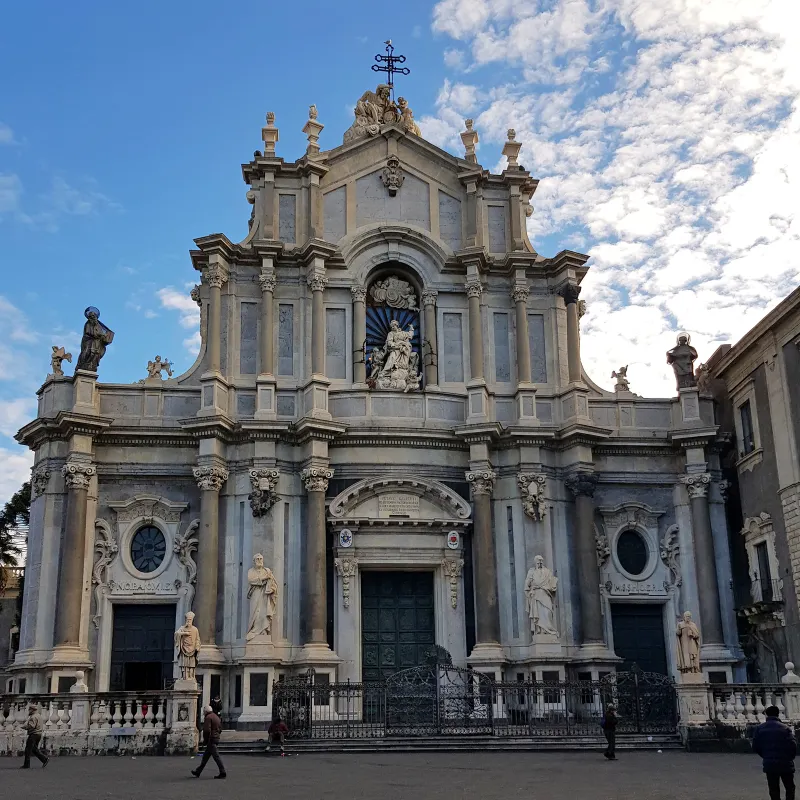Catania Cathedral’s ornate grey-stone façade with columns, statues, arched windows and a central doorway.