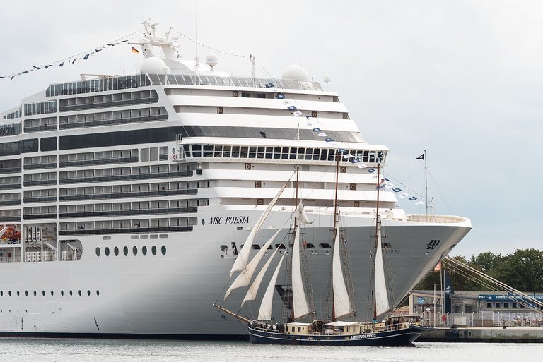 A massive cruise ship next to a tall ship.