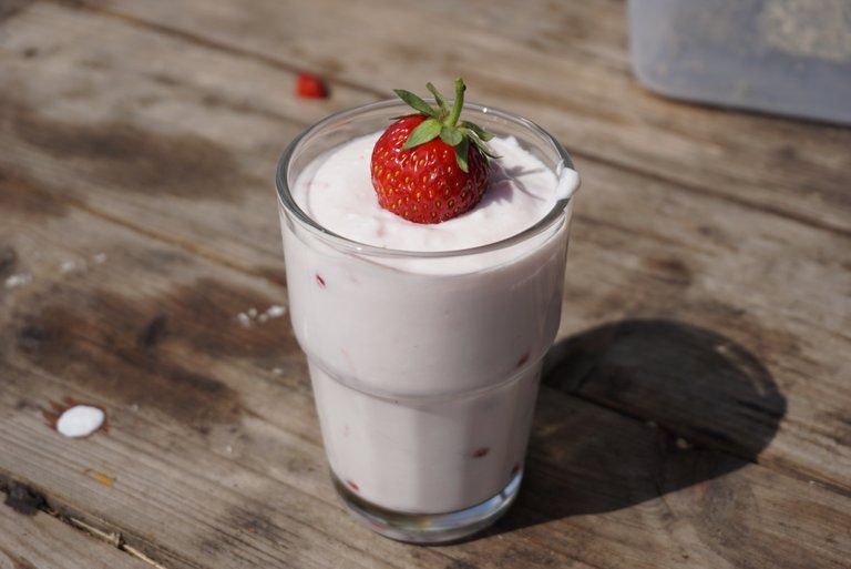 Small glass filled with yoghurt, which contains fresh chopped strawberries. On the yoghurt is a very good-looking strawberry on the whole decorated with a stalk approach decorative.