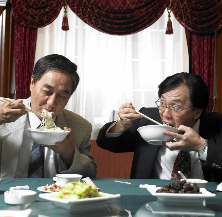 Two-mature-businessmen-eating-noodles-at-banquet-table.jpg