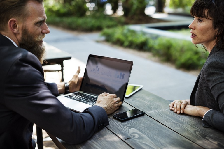 “Two businesspeople talking at a table over a laptop with line charts” by rawpixel on Unsplash