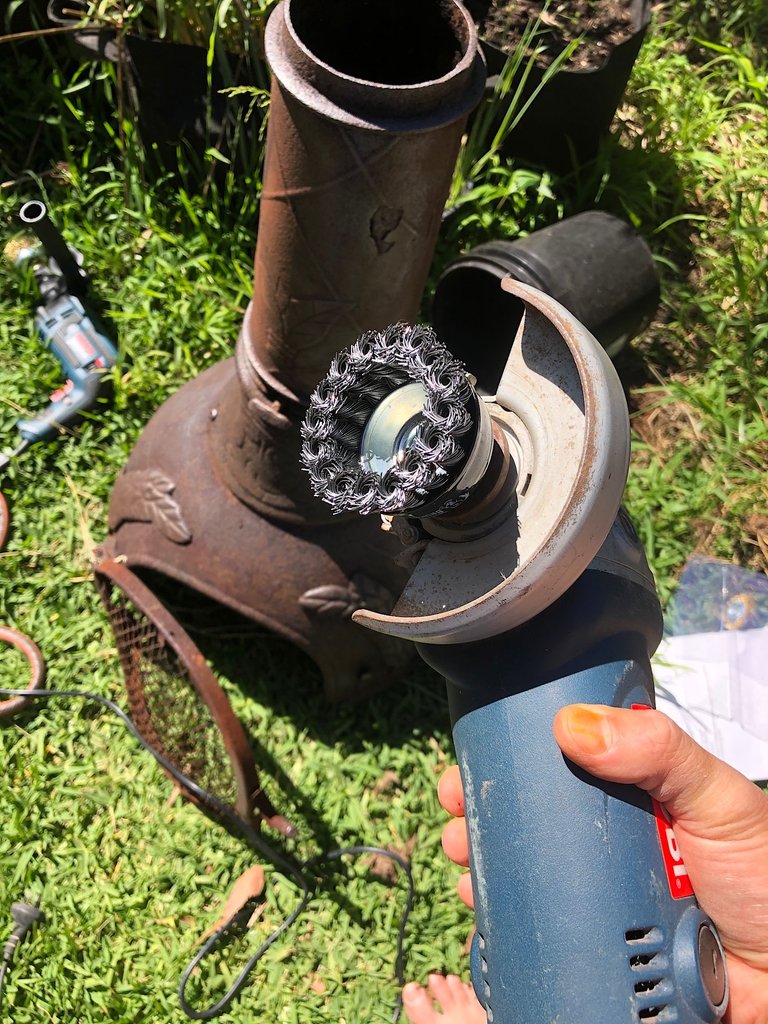 Scrubbing the rusty chimenea with a angle grinder and cup brush