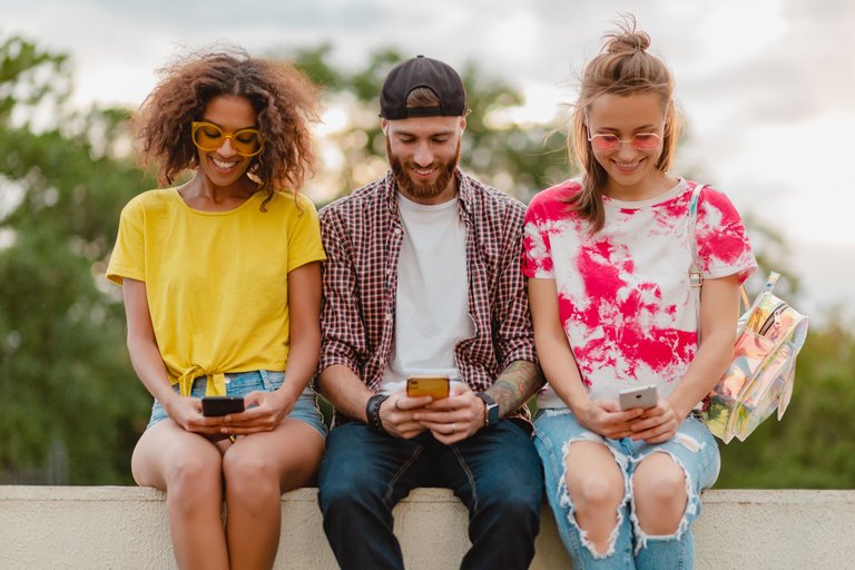 happy-young-company-of-smiling-friends-sitting-park-using-smartphones.jpg