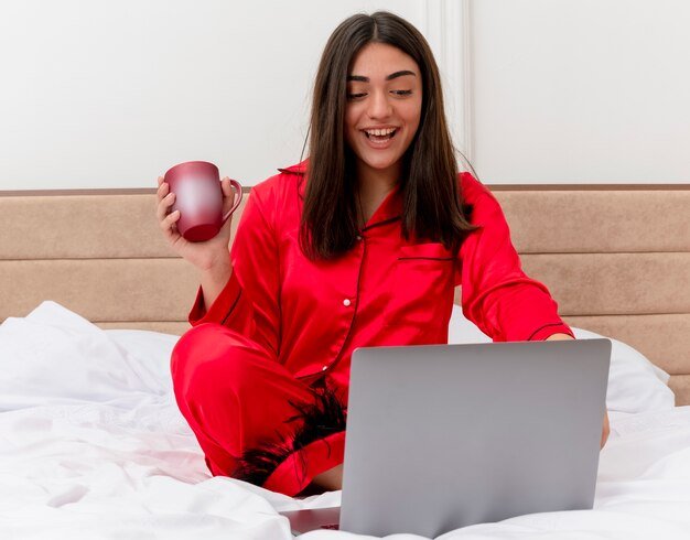 young-beautiful-woman-red-pajamas-sitting-bed-with-laptop-cup-coffee-happy-positive-smiling-cheerfully-bedroom-interior-light-background_141793-45478.jpg