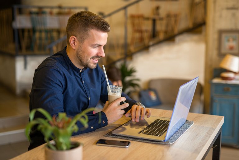 sonriente-joven-trabajando-en-la-computadora-en-el-acogedor-restaurante-bar-cafeteria.jpg
