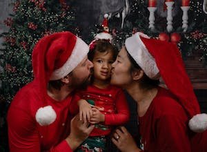 free-photo-of-parents-kissing-their-little-daughter-on-the-cheeks-dressed-in-christmas-pajamas-and-santa-hats.jpeg