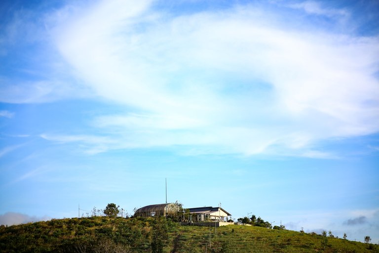 A small house on top of a hill with a beautiful cloud above.