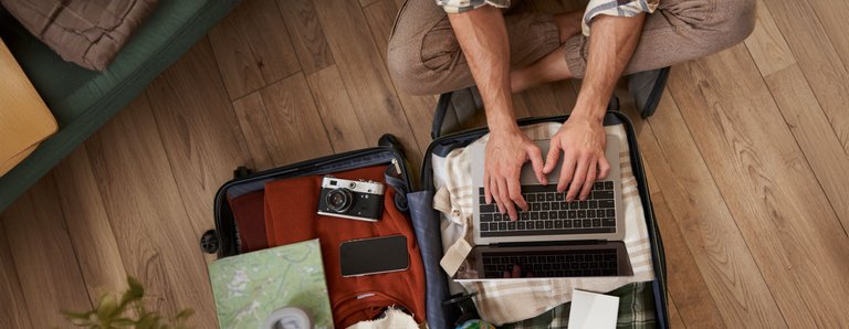 close-up-tourist-hands-typing-laptop-opened-suitcase-with-clothes-holiday-man-packs-luggage.jpg