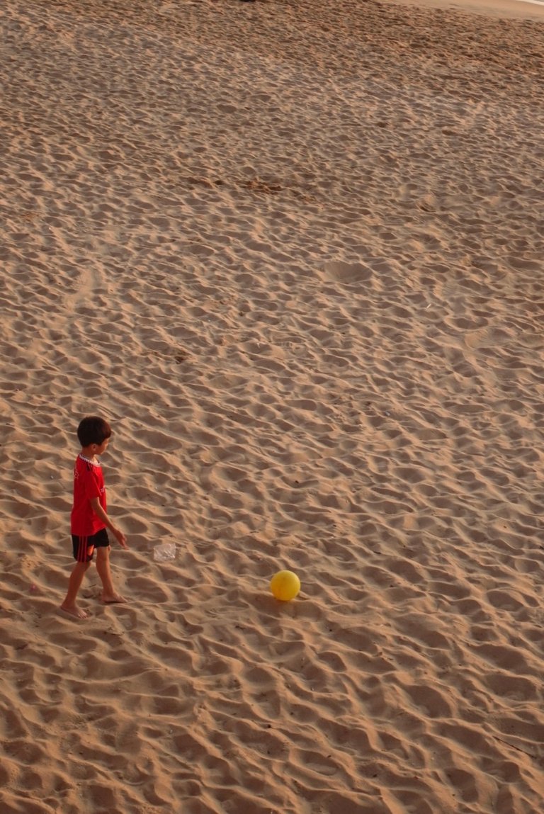 A boy playing soccer on the beach