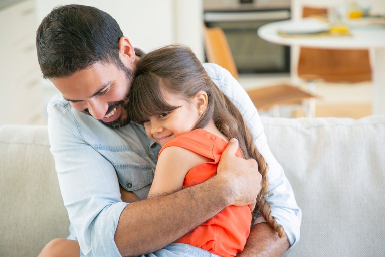 joyful-dad-sitting-with-his-little-girl-on-couch-hugging-and-cuddling-her.jpg