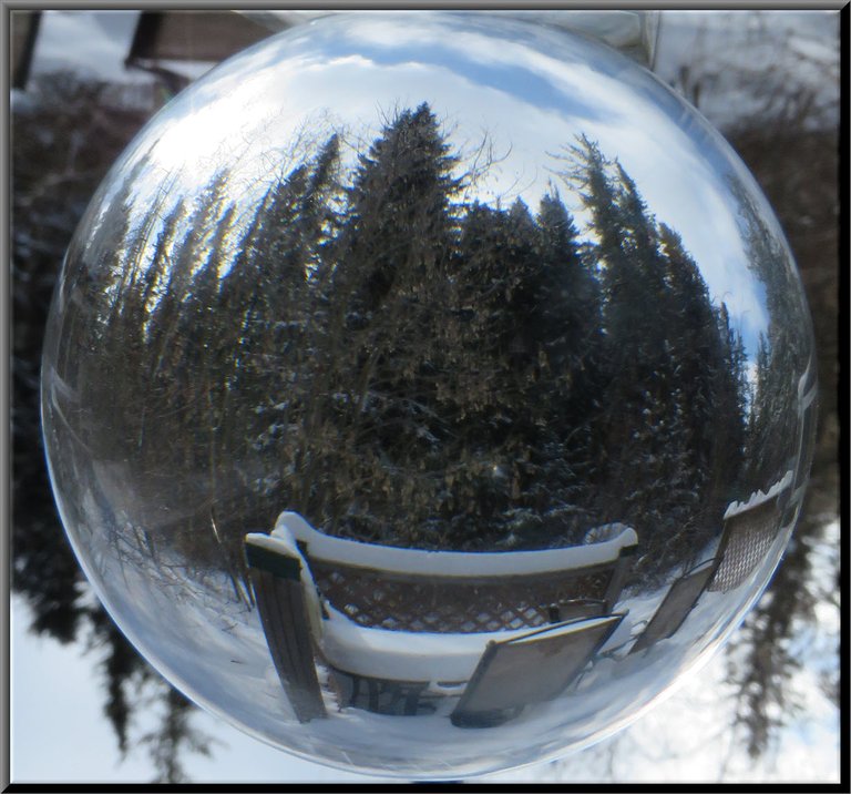 reflection in crystal ball of snowy deck chairs and table with snowy evergreens in background.JPG