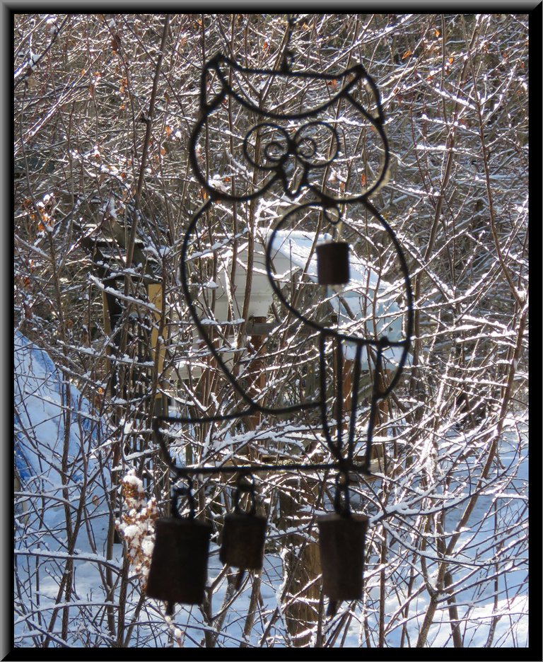 outline of owl wind chime with light snow covered bushes behind.JPG
