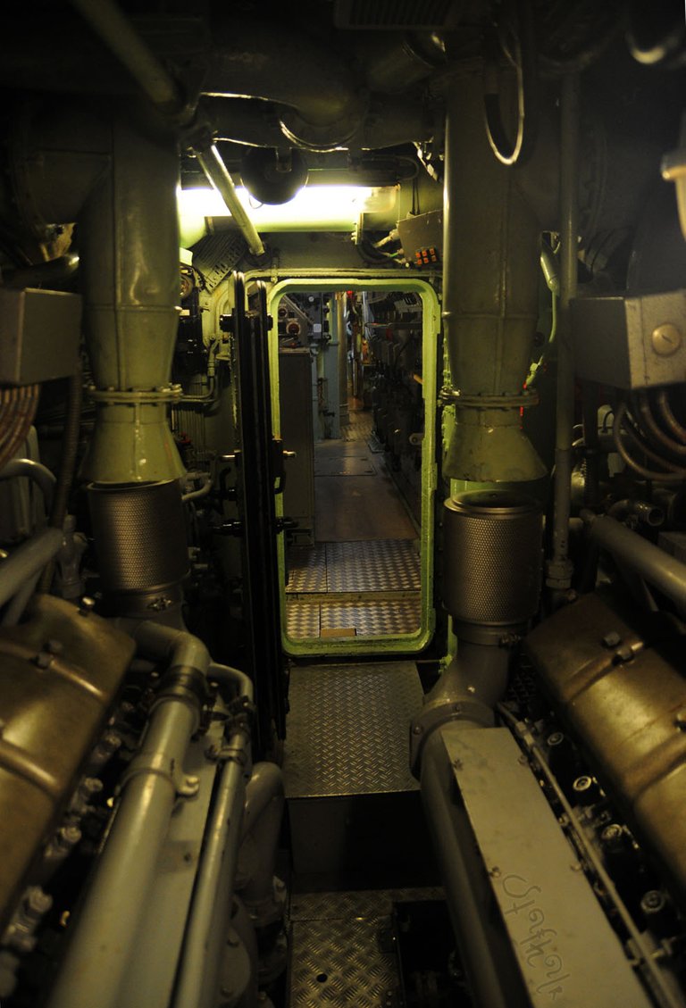 Widok z maszynowni w stronę dziobu okrętu. Po bokach siniki wysokoprężne // View from the engine room towards the bow of the ship. Diesel engines on the sides