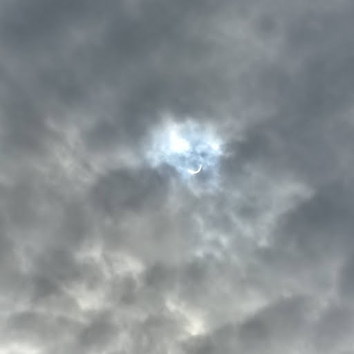 The sun peaking thru the clouds. You can see a little bit of eclipse.