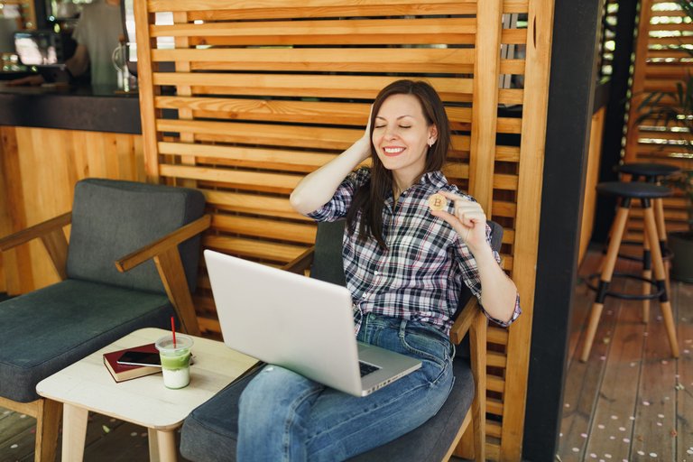 woman-outdoors-street-coffee-shop-cafe-sitting-with-laptop-pc-computer-hold-bitcoin-metal-coin-golden-color.jpg