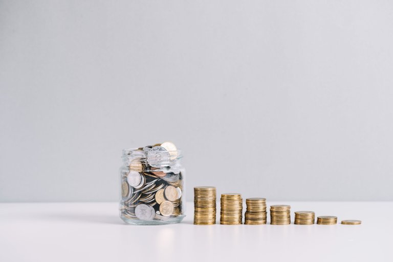 glass-jar-full-of-money-in-front-of-decreasing-stacked-coins-against-white-background.jpg