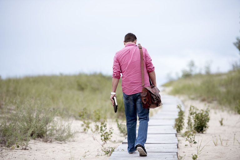 male-holding-notebook-walking-wooden-pathway-middle-sandy-surface.jpg