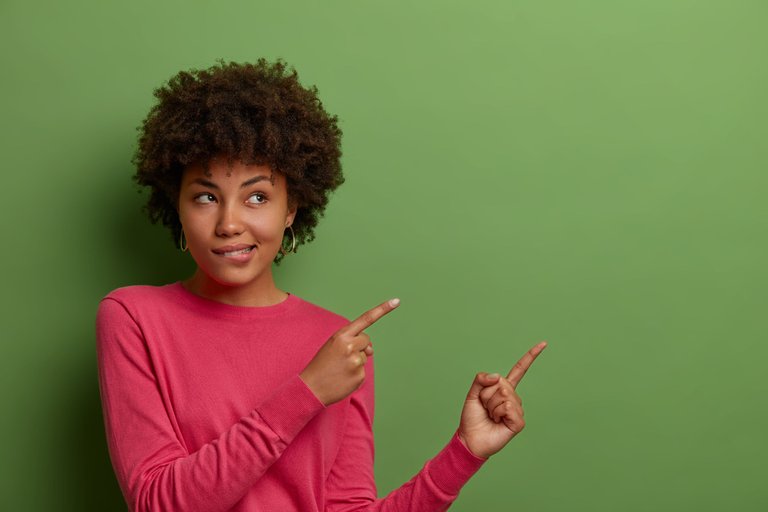 indoor-shot-curious-african-american-woman-bites-lips-sees-something-good-indicates-fingers-blank-space-green-wall-shows-place-your-product-company-banner-promotion.jpg