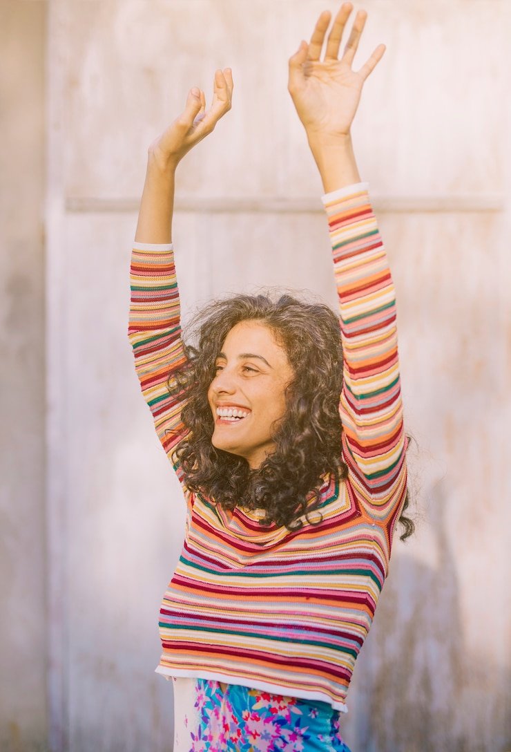 retrato-mujer-joven-sonriente-levantando-sus-brazos-contra-pared_23-2148066874.jpg