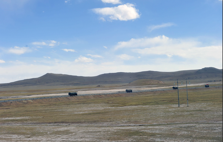 Truck convoy driving through the Tibetan Plateau along the railway