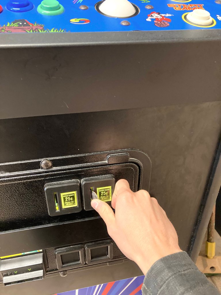 Public domain stock photo -- closeup image of a person's hand putting quarters into an arcade machine