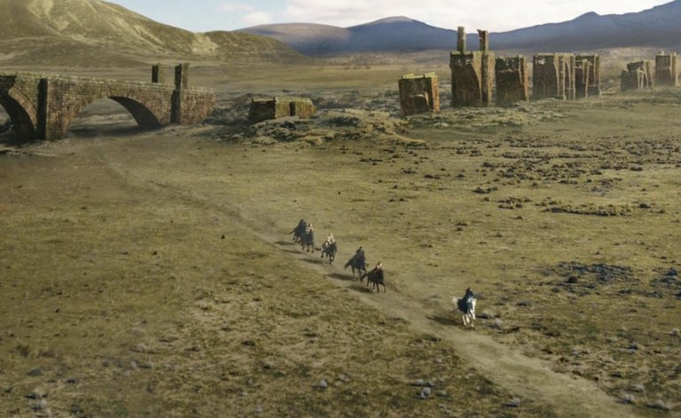 Screenshot from Wheel of Time Episode 2: Shadows Waiting showing the 6 companions traveling by horseback, ruins of an ancient aqueduct in the background