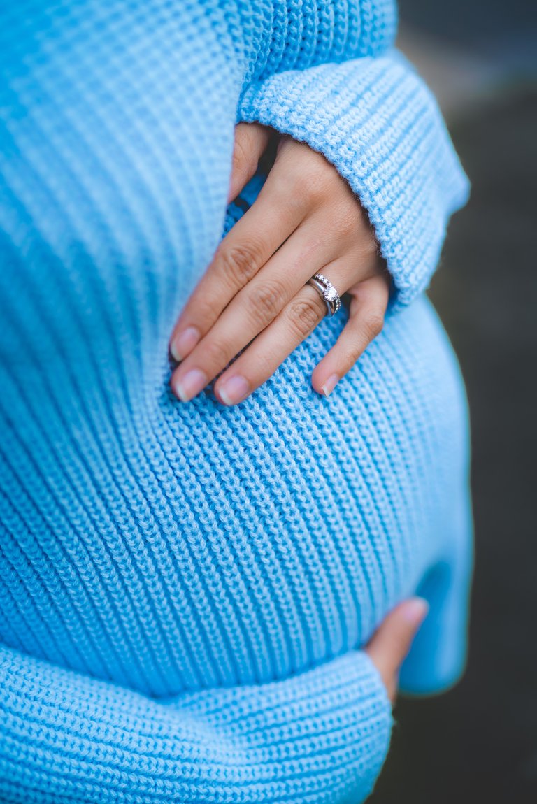 woman holding her belly while wearing blue knit sweater