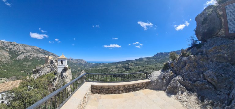 The King’s Castle on the left, the Mediterranean Sea in the background and a commemorative plaque on the upper right corner, on which the following sentence can be read, translated into four languages: ”Wanderer, stop a while and think of the marvellous works of God and of your short passage on Earth. Guadalest begs you to respect its deads.”