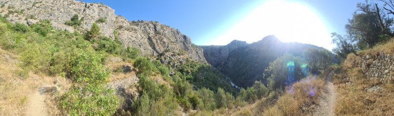 Panoramic of the bottom of the ravine in the shadow and the powerful sun on the hillside path.