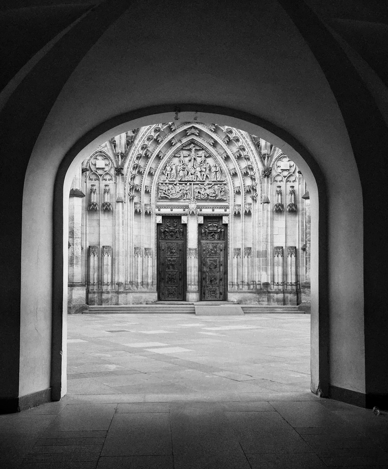 St. Vitus Cathedral’s ornate entrance framed through a dark stone arch in Prague.