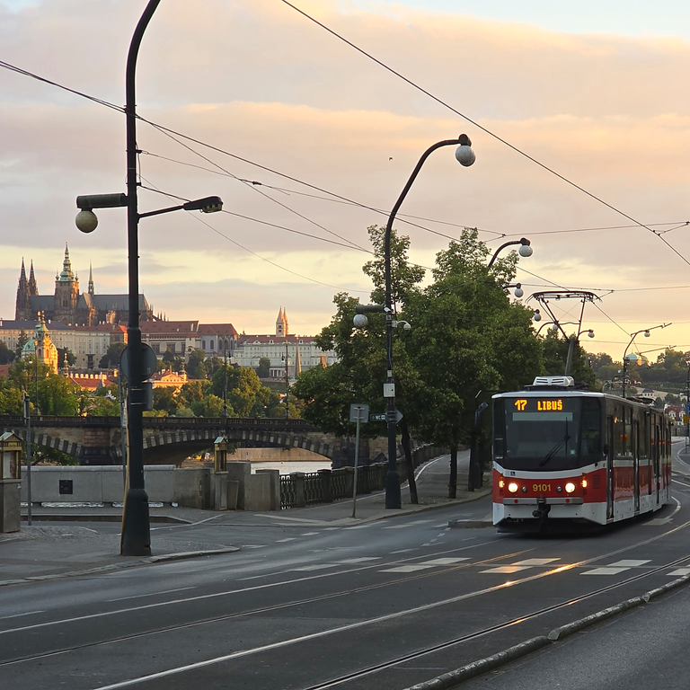 Red tram on Masarykovo nábřeží with Prague Castle and the Vltava riverbank in the background.