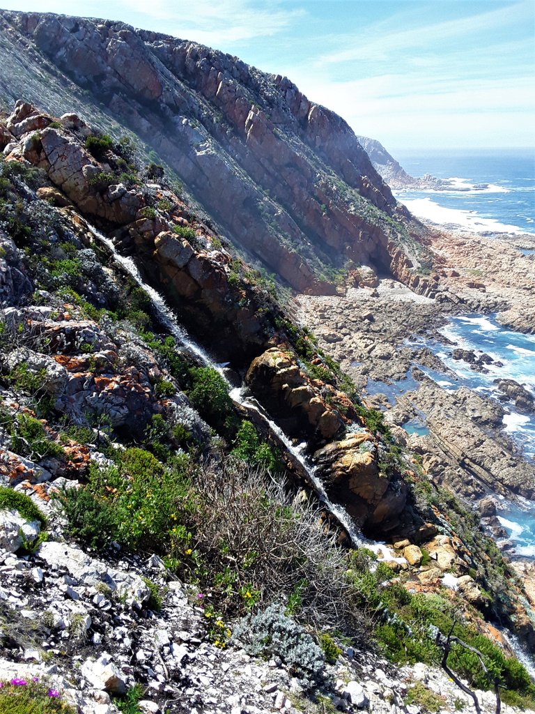 A seasonal river of rain water pours down the cliff toward the sea below. Notice the awesome cave down there