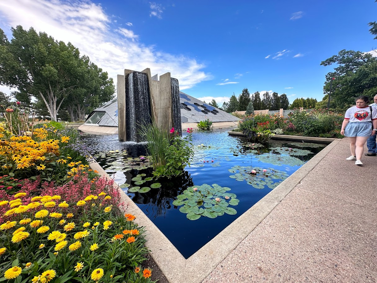 Where Nature Meets Architecture: Water mirrors the sky beside a bloom-speckled path, with modernity and tranquility in perfect harmony.