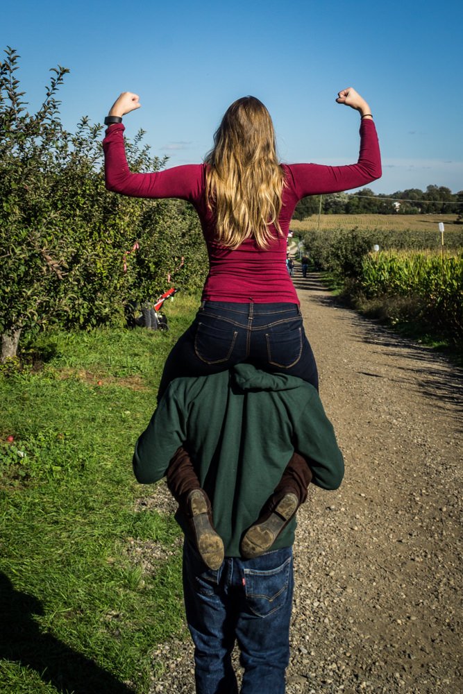 Woman on someones shoulders with arms making a strength sign