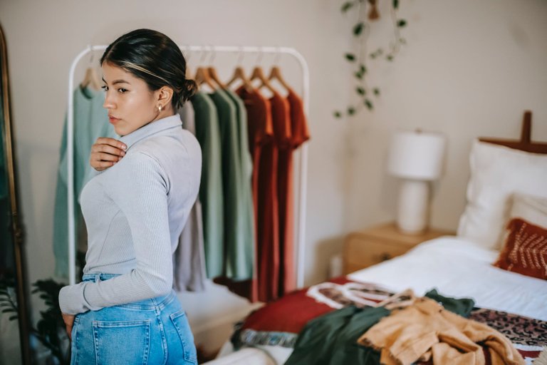 ethnic female demonstrating and selecting clothes in bedroom