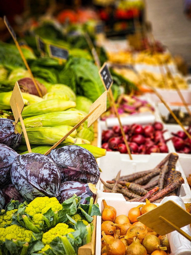 Selection of purple and green vegetables at an outdoor market in Copenhagen, including broccoli and kale varieties