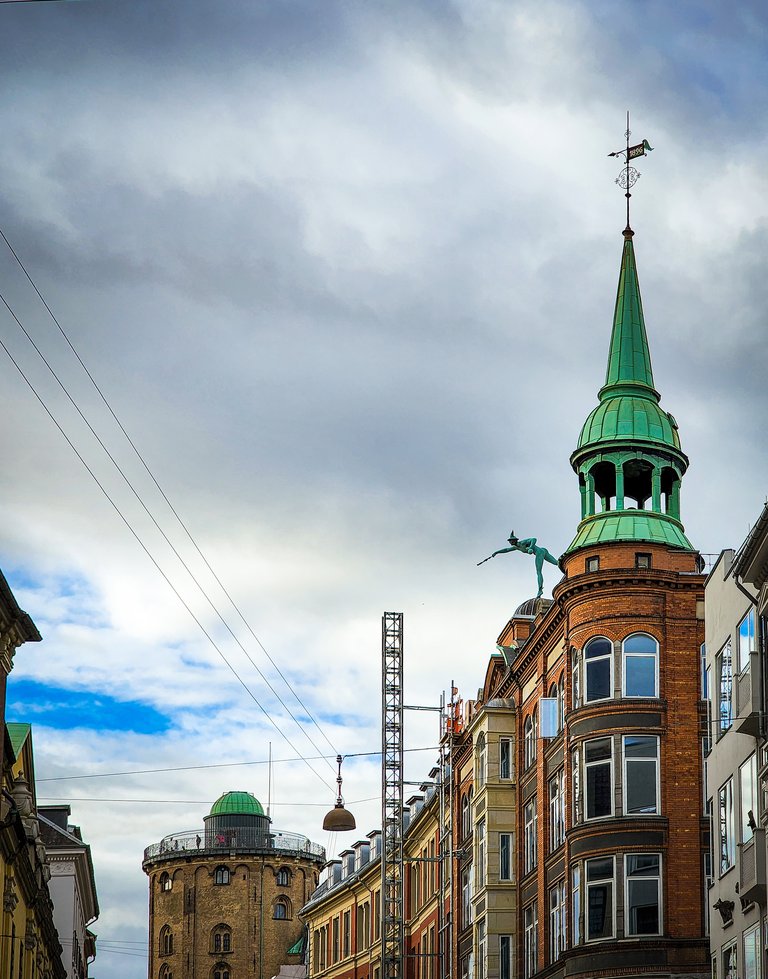 Historic building with a distinctive green spire against a partly cloudy sky in Copenhagen