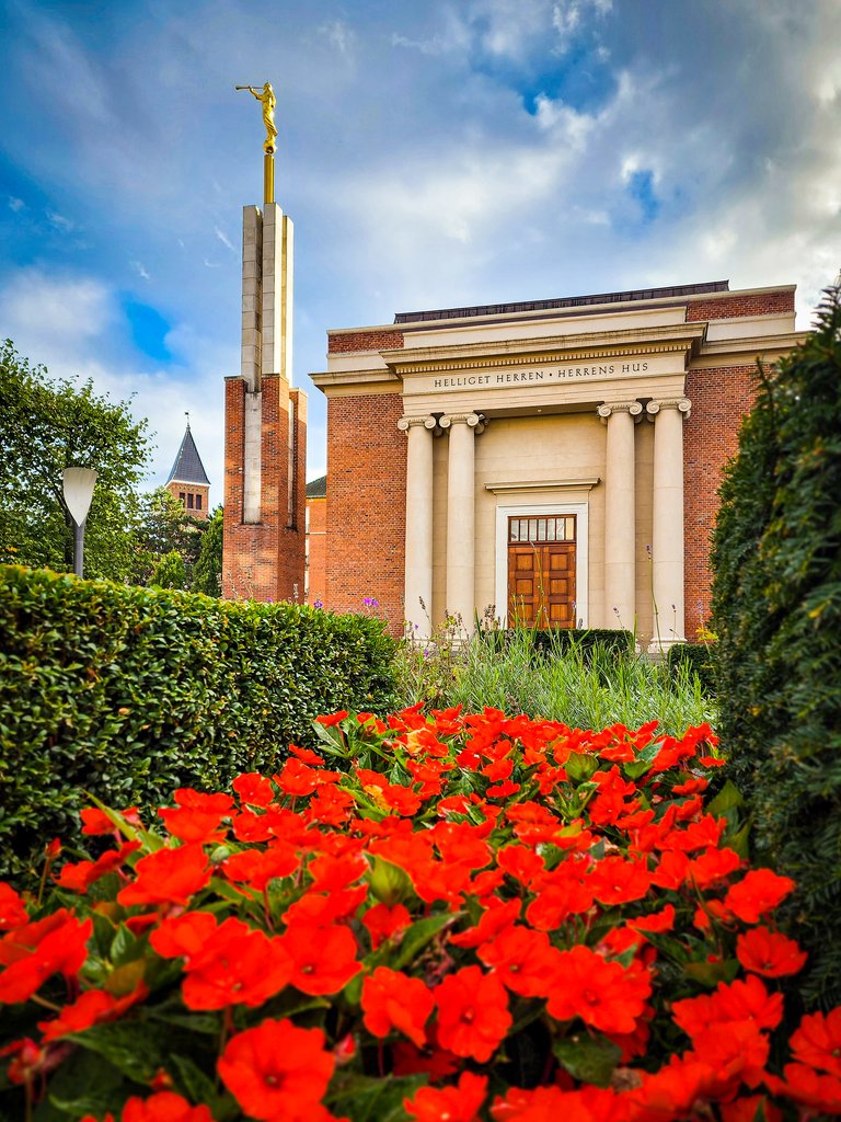 LDS temple in Denmark with lush landscaping and red flowers in the foreground