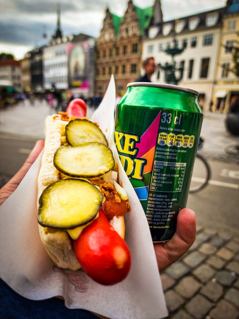 Holding a Danish hot dog with a drink in Copenhagen's city square