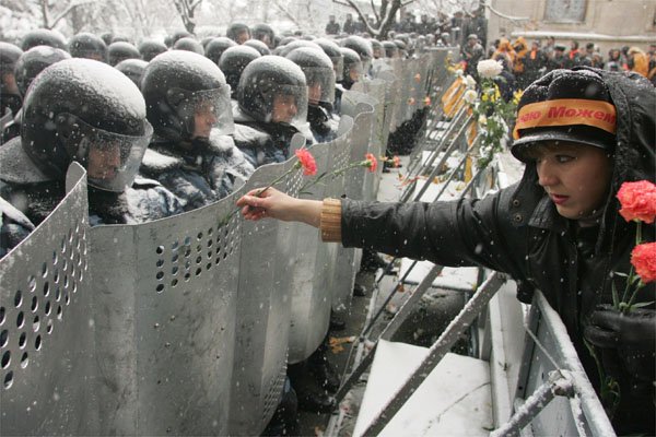 Ukrainian woman places carnations into shields of anti-riot policemen standing outside the ...