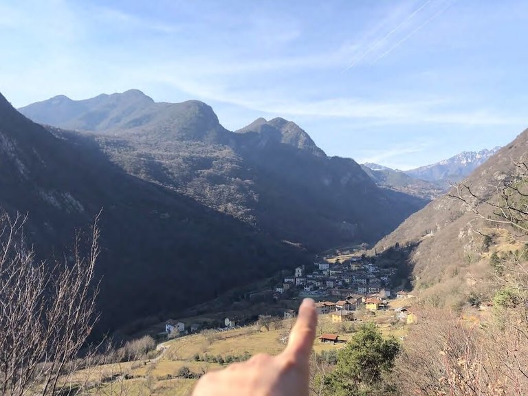 Ausblick in ein Bergtal mit Finger, der in Richtung eines Dorfes zeigt