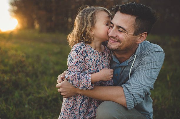 girl-kissing-father-on-cheek-in-field-picture-id551986299.jpg