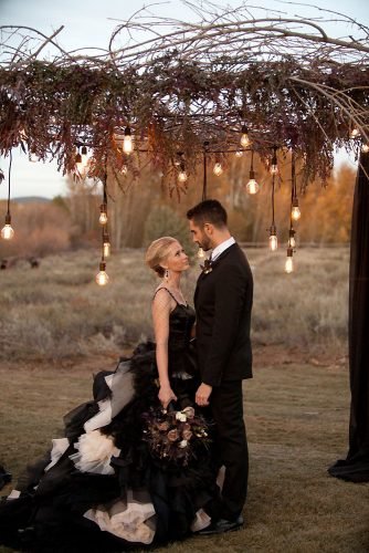 halloween-wedding-ideas-photo-shoot-the-bride-and-groom-in-a-black-dress-with-a-veil-under-an-arch-of-branches-with-bulbs-todd-nichols-photography-334x500.jpg