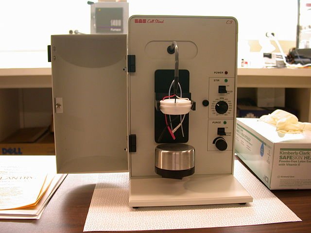 A modern cell stand for electrochemical research. The electrodes attach to high-quality metallic wires, and the stand is attached to a potentiostat/galvanostat (not pictured). A shot glass-shaped container is aerated with a noble gas and sealed with the Teflon block.