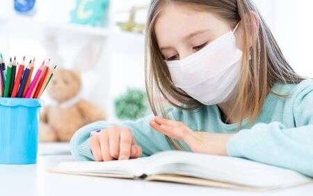 Cute Schoolgirl In Medical Face Mask Studying At Home Stock Photo ...