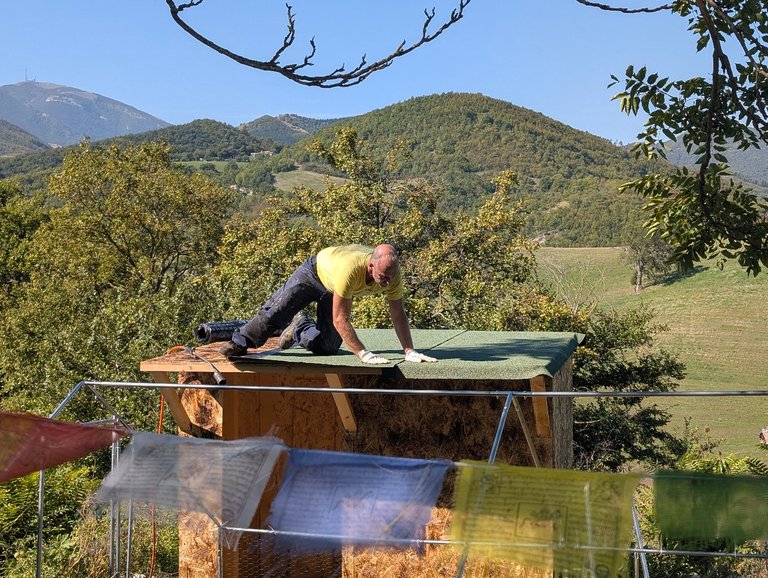 PHOTO: roofing work in progress on the compost toilet, hills and prayer flags in the background