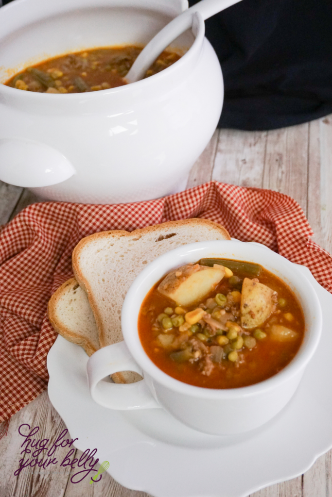 hamburger soup in white cup with a saucer and slice of bread