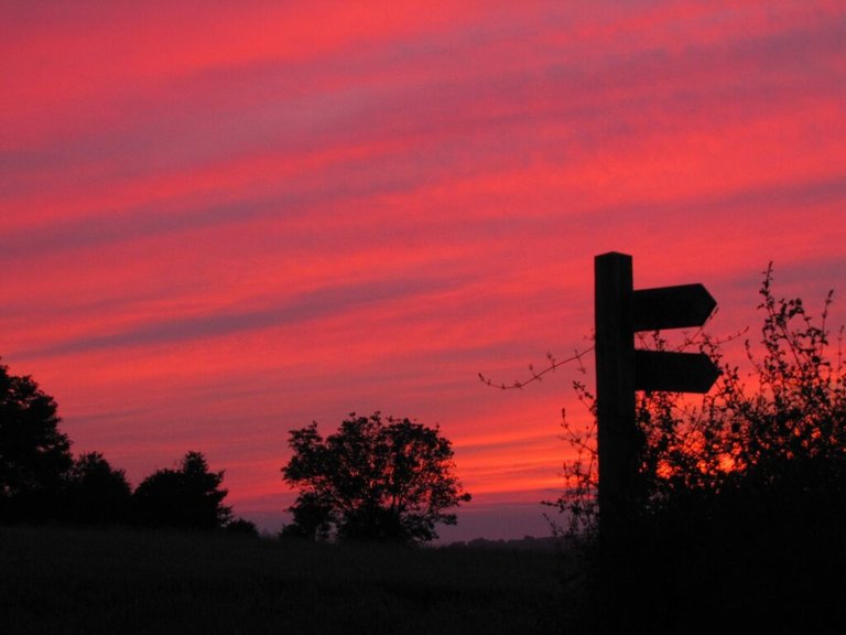 A signpost silhouetted against a vivid sunset - Why do I travel? To see more sunsets and sunrises, in as many places as possible.